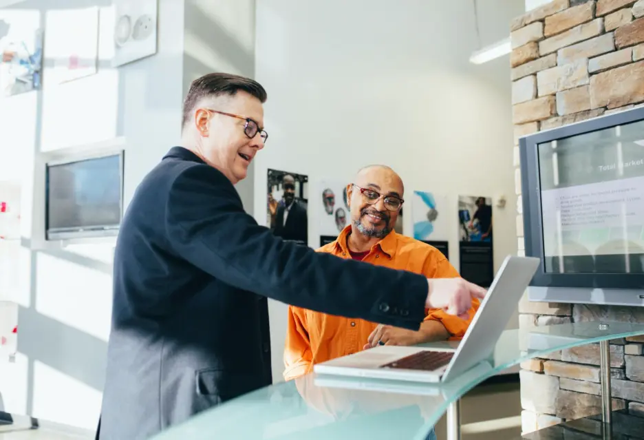 Two business professionals collaborating on a laptop to explore Zlendo Realty AI software sales and consulting opportunities