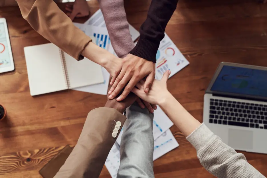 Diverse team joining hands over business charts symbolizing global partnership and collaboration with Zlendo Realty